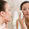 A young woman in a bathroom is looking at her reflection in the mirror while gently drying her face with a towel.