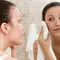 A young woman in a bathroom is looking at her reflection in the mirror while gently drying her face with a towel.