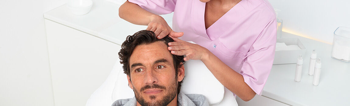A healthcare professional in a pink uniform is treating a man's scalp while he relaxes in a clinical setting.