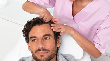 A healthcare professional in a pink uniform is treating a man's scalp while he relaxes in a clinical setting.