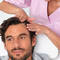 A healthcare professional in a pink uniform is examining the scalp of a man lying down on a treatment table.