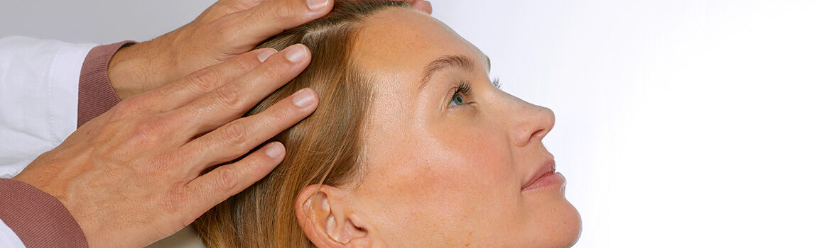 A healthcare professional gently examines the scalp of a woman lying down, focusing on her hair and head.