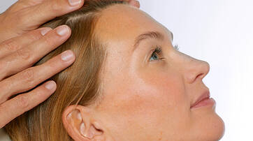 A healthcare professional gently examines the scalp of a woman lying down, focusing on her hair and head.