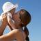 A woman holds a baby in the air and gives them a kiss against a clear blue sky.