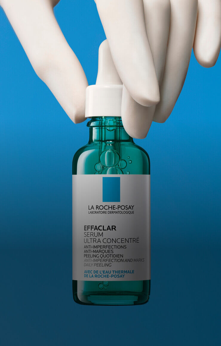 Un flacon de serum Effaclar de La Roche-Posay, tenant par une main, sur un fond bleu.