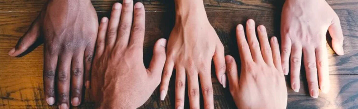 A variety of hands with different skin tones are placed on a wooden surface, showcasing diversity and unity.