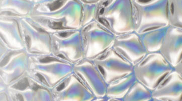 An abstract surface featuring shiny, irregularly shaped bubbles with a subtle iridescent sheen, reflecting various colors.