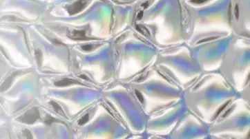 An abstract surface featuring shiny, irregularly shaped bubbles with a subtle iridescent sheen, reflecting various colors.