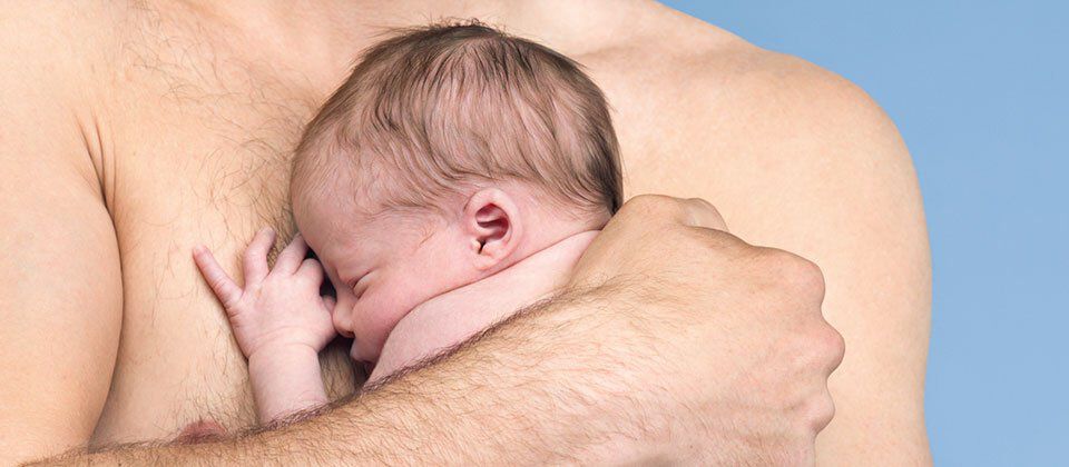 A close-up of a newborn baby nestled against a man's chest, both appearing calm and content. The background is a soft blue.
