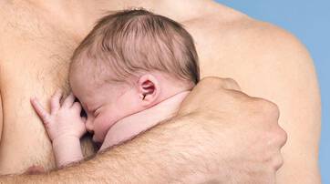 A close-up of a newborn baby nestled against a man's chest, both appearing calm and content. The background is a soft blue.