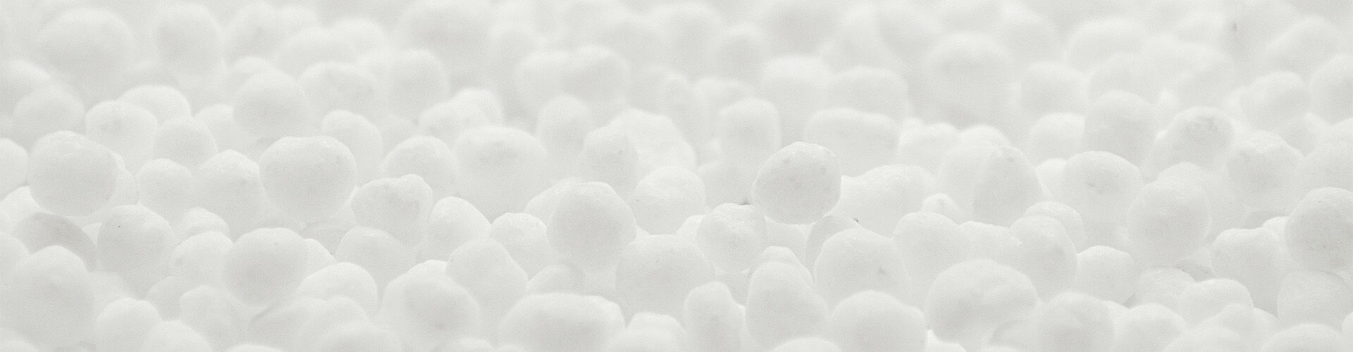 A close-up view of numerous small, white spherical particles resembling polystyrene beads or snowflakes, creating a soft and textured surface.