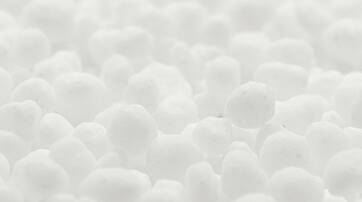 A close-up view of numerous small, white spherical particles resembling polystyrene beads or snowflakes, creating a soft and textured surface.