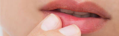 Close-up of a person's lips with a finger gently touching them.