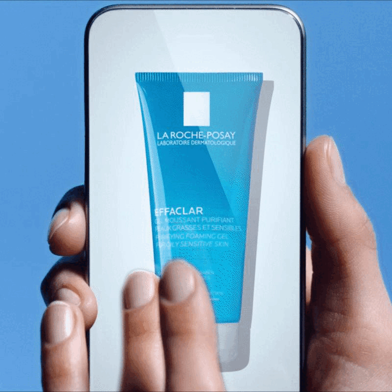 Un smartphone affiche un tube de gel nettoyant La Roche-Posay Effaclar pour peau grasse et sensible, sur fond bleu.