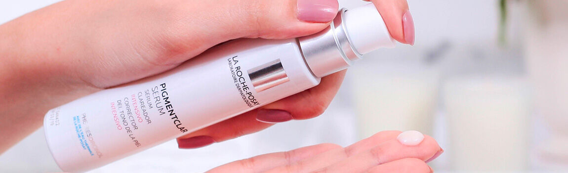 A hand holding a bottle of La Roche-Posay Pigmentclar serum, with a small amount of the product dispensed onto the palm.