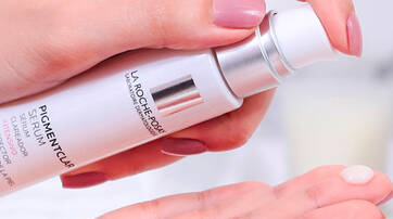 A hand holding a bottle of La Roche-Posay Pigmentclar serum, with a small amount of the product dispensed onto the palm.