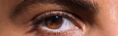 Close-up of a human eye, showcasing brown iris and detailed eyelashes against a smooth skin background.