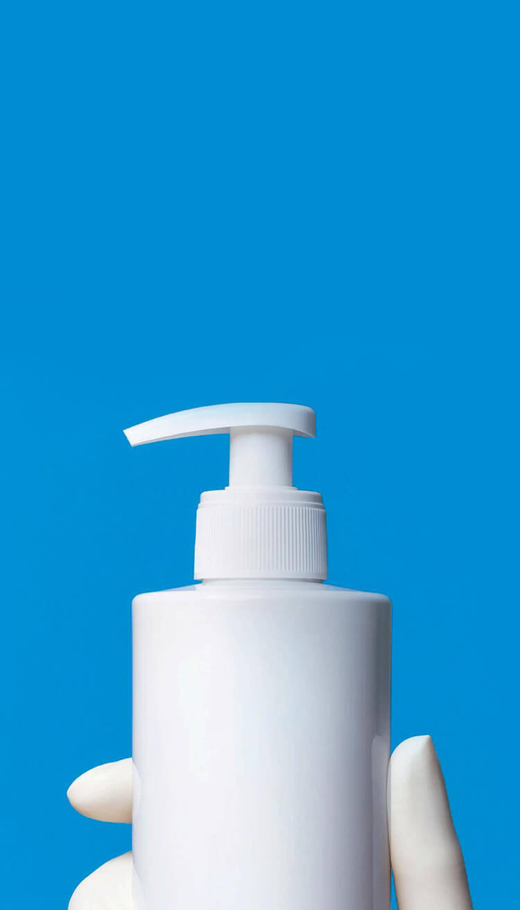 Flacon de lotion blanche a pompe, tenu par une main, sur fond bleu.