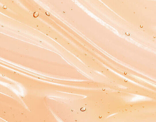 A smooth, wavy surface in a soft peach color with small droplets of water glistening on it.