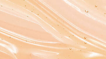 A smooth, wavy surface in a soft peach color with small droplets of water glistening on it.
