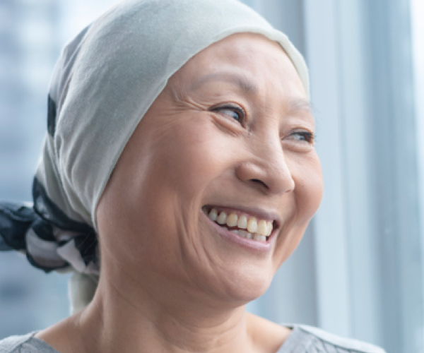 Une femme souriante portant un foulard sur la tete, assise pres d'une fenetre.