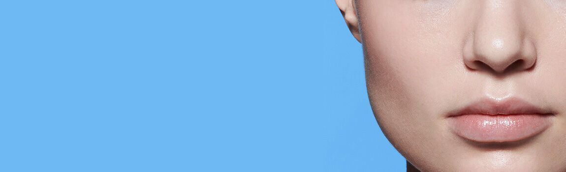 Close-up of a person's lips and jawline against a solid blue background. The skin appears smooth and luminous.