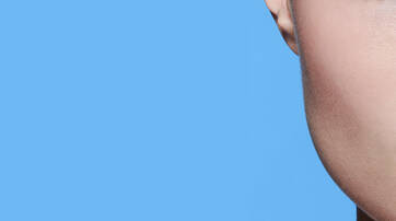 Close-up of a person's lips and jawline against a solid blue background. The skin appears smooth and luminous.