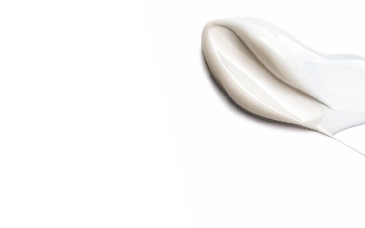 Une texture creme blanche etalee sur un fond blanc, avec quelques gouttes eclaboussees a proximite.