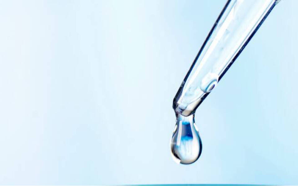 Une pipette en verre verse une goutte d'eau sur un fond bleu clair.