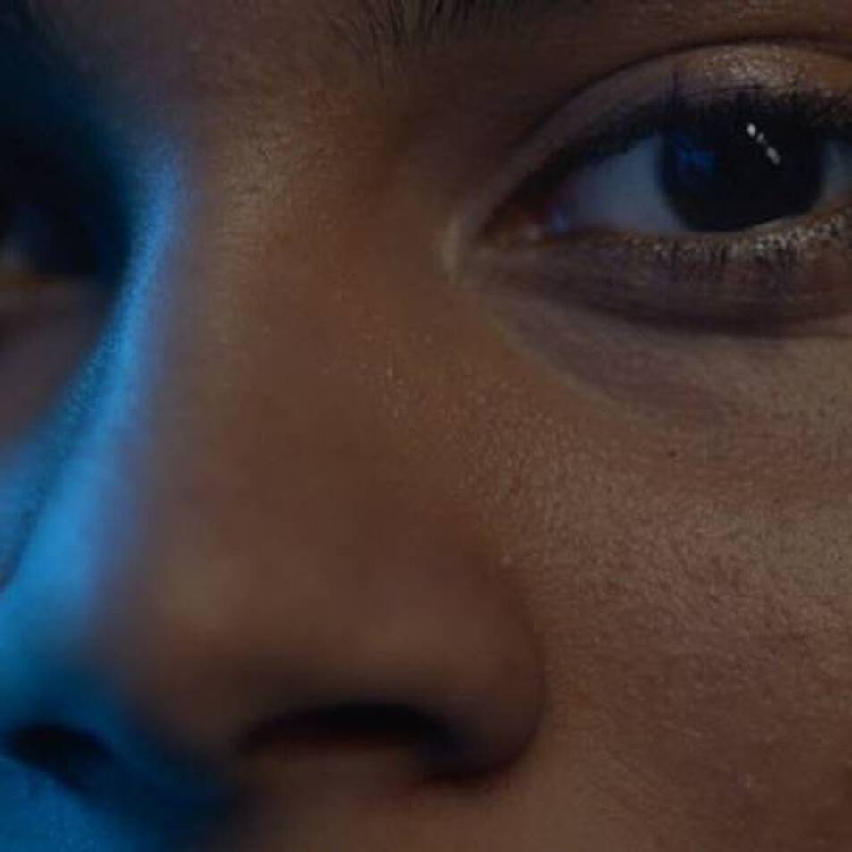 Close-up of a young person's face, focusing on their expressive eyes and skin texture, with a soft blue light illuminating the scene.