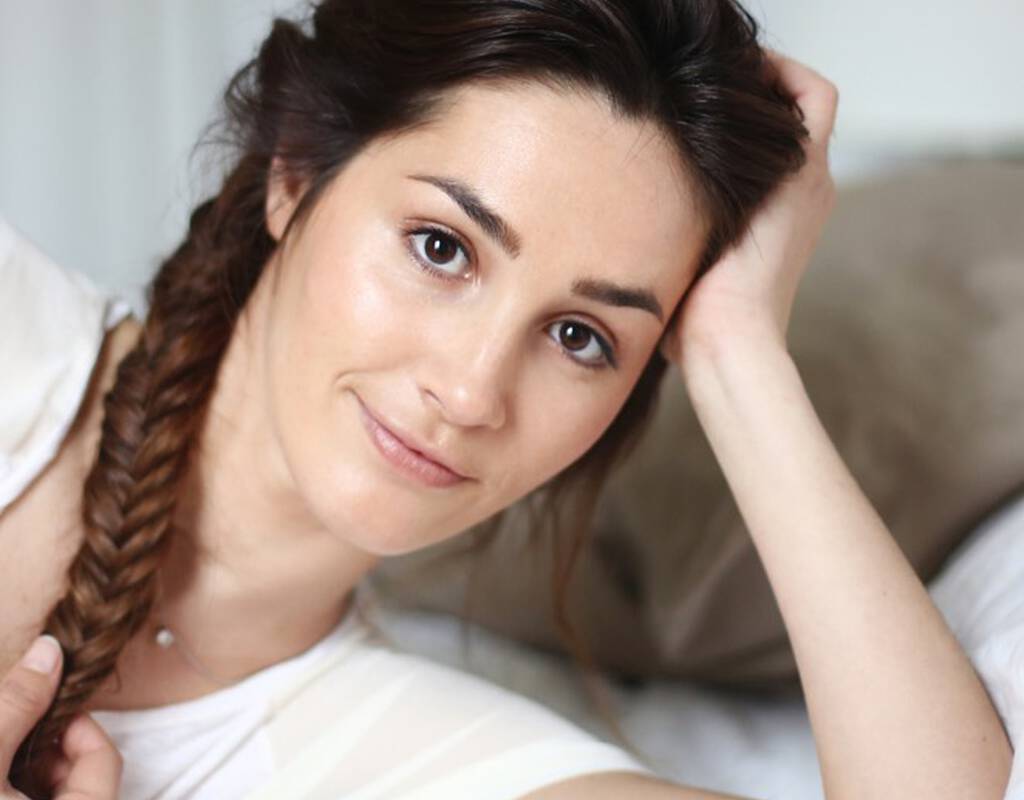 Une femme souriante avec les cheveux tresses, posant sur un lit.