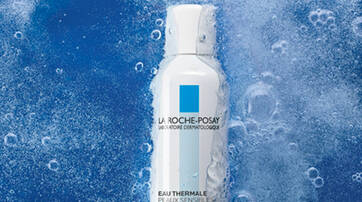 A white spray bottle of La Roche-Posay thermal water against a blue background with bubbles surrounding it.