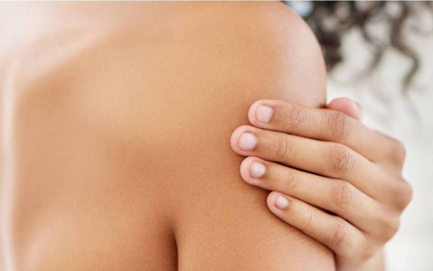 Une personne de dos, mettant une main sur son epaule, avec une peau caramel et des cheveux boucles.