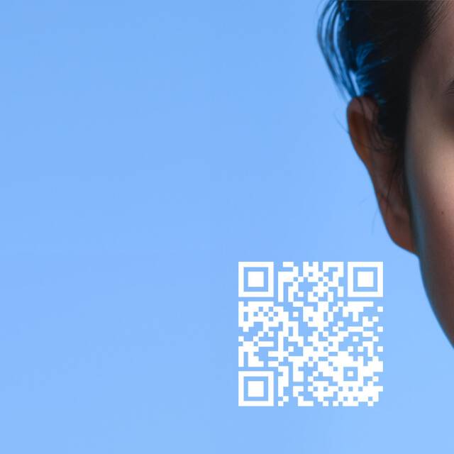 Une personne regarde l'objectif avec un visage partiellement en bleu numerique, accompagnee d'un code QR sur fond bleu. Le mot "SPOTSCAN" est visible a gauche.
