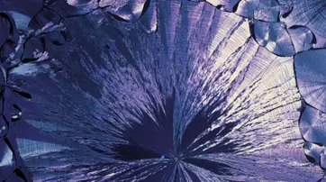 Close-up image of vibrant, iridescent crystalline structures with a mix of purples and silvers, displaying intricate patterns and textures.