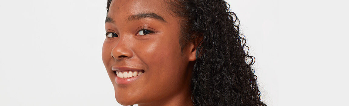 A young woman with curly hair smiles gently, facing slightly to the right against a neutral background.
