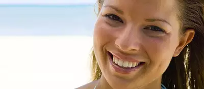A woman smiling at the camera with a beach and ocean in the background.