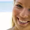 A woman smiling at the camera with a beach and ocean in the background.