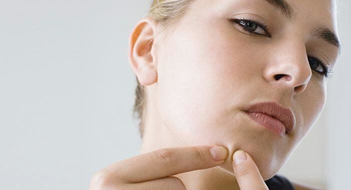 A close-up of a young woman examining her chin while gently touching a blemish on her skin.