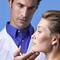 A healthcare professional examining a woman's jawline against a light blue background.