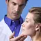 A healthcare professional examining a woman's jawline against a light blue background.