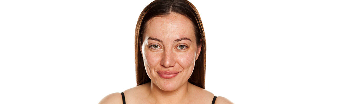 A young woman with long, straight brown hair smiles softly at the camera, wearing minimal makeup and a black top against a plain white background.