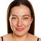 A woman with long brown hair smiles directly at the camera, displaying her natural skin without makeup against a plain white background.