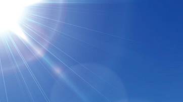 A bright sunburst shines against a clear blue sky, creating lens flares and light rays.