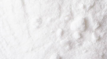 Close-up of white granulated sugar, showcasing its fine texture and small crystals against a soft surface.