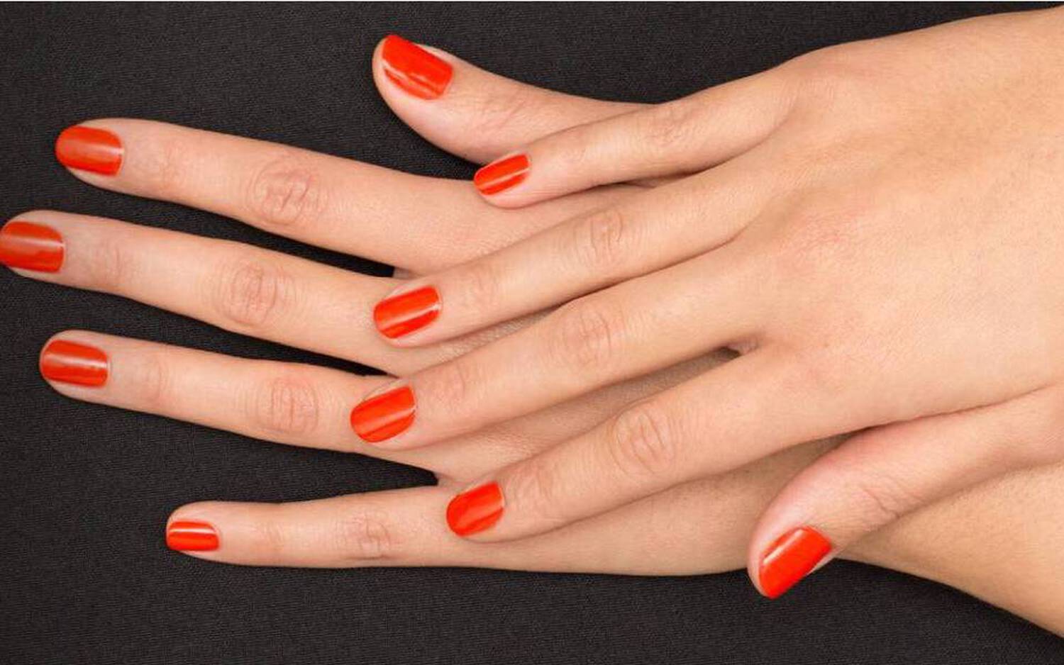 Deux mains aux ongles vernis en rouge reposent sur un fond noir.