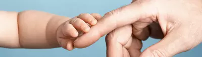 A close-up image of a baby's hand grasping an adult's finger, highlighting the tenderness and connection between them. The background is a soft blue.
