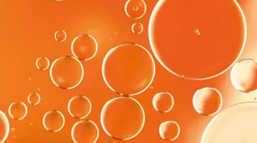 Close-up image of translucent orange bubbles floating against a vibrant orange background.