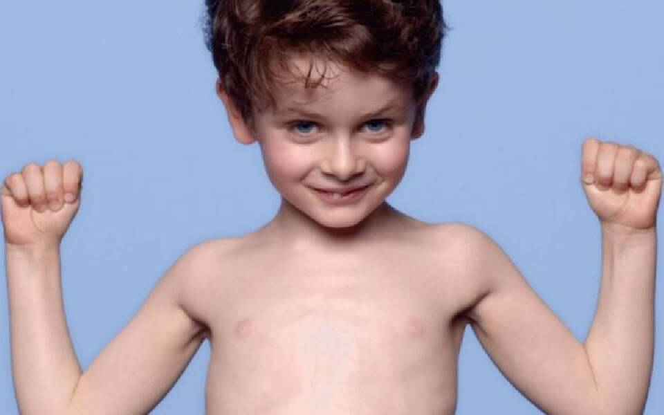 Un garcon souriant, torse nu, fait des gestes de force avec les bras leves, sur un fond bleu clair.