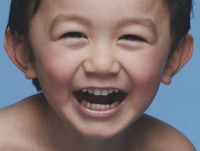 Un jeune garcon souriant, torse nu, sur un fond bleu.
